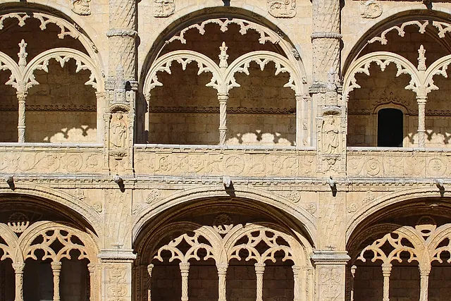 Vista cercana de las arcadas de dos plantas del claustro, con arcos tallados como encaje y esbeltas columnas de piedra dorada y cálida