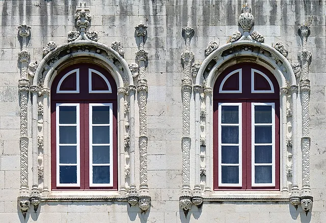 Dos ventanas de arco con marcos rojo oscuro abiertas en un muro de piedra clara y rodeadas de columnas retorcidas elaboradamente talladas y ornamentos de piedra