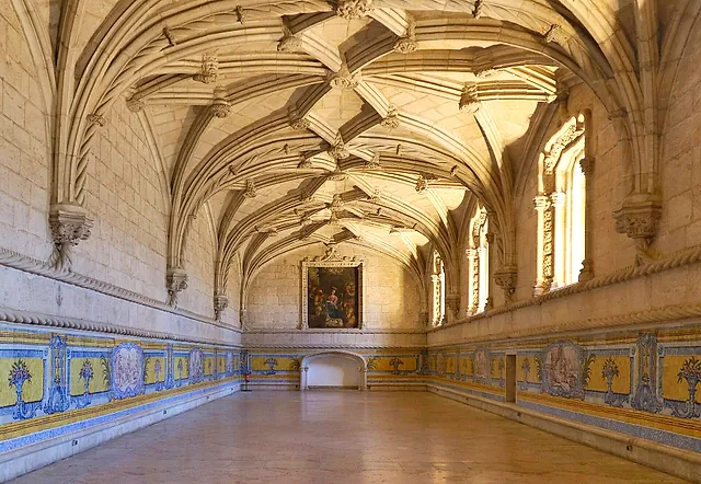 El largo refectorio con bóveda de nervaduras, paneles de azulejos azules y amarillos en la parte baja de las paredes y una pintura al fondo, iluminado por la luz del sol de las ventanas