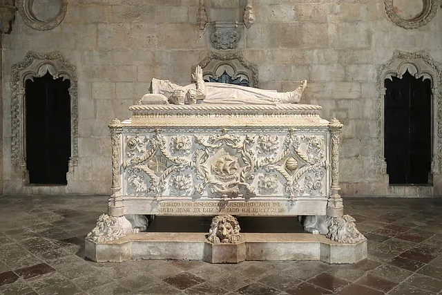 Una tomba di marmo bianco scolpita con una nave e motivi vegetali, sormontata da una figura distesa e poggiata su leoni scolpiti, tra due nicchie scure a punta su un pavimento di pietra