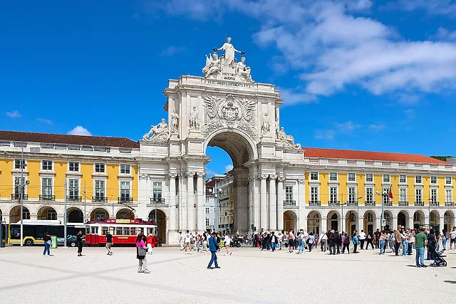 L'Arco da Rua Augusta con un gruppo di statue in cima, incorniciato dagli edifici a portici gialli e bianchi di Praça do Comércio sotto un cielo azzurro